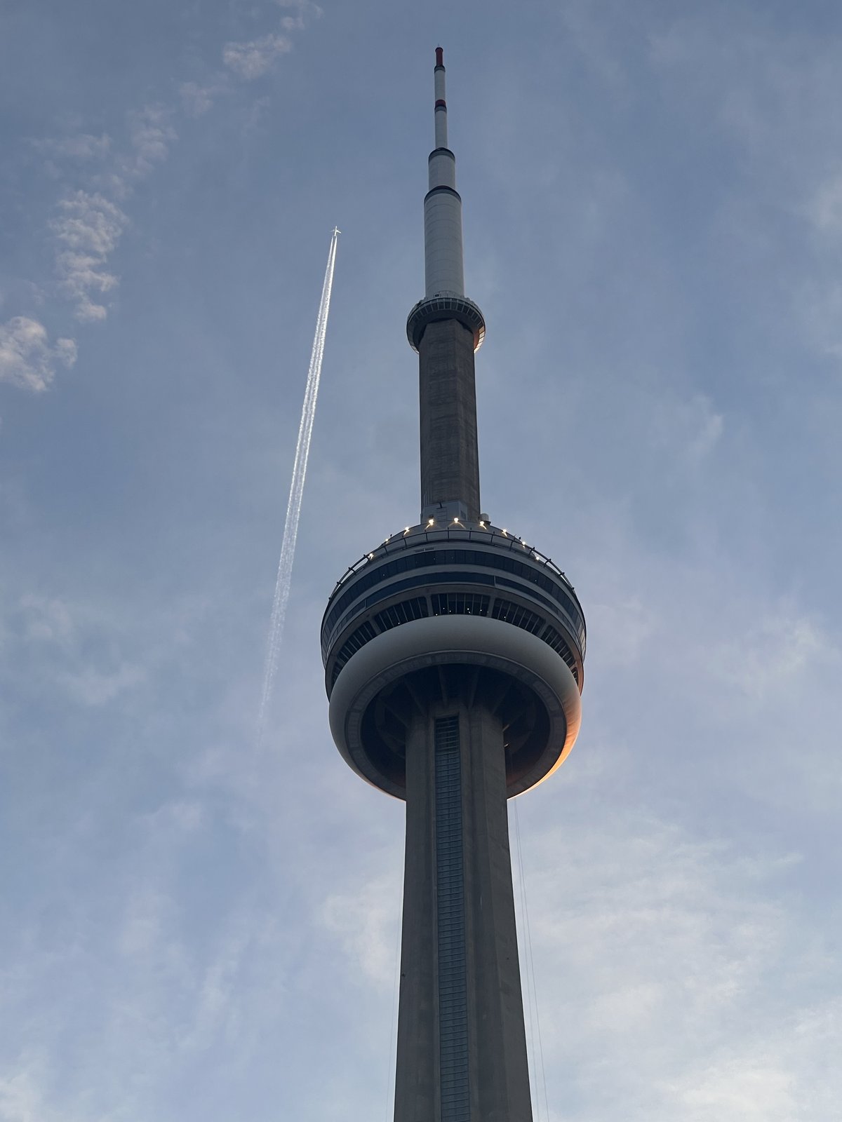 The CN Tower at dusk with a jet contrail crossing the sky beside it