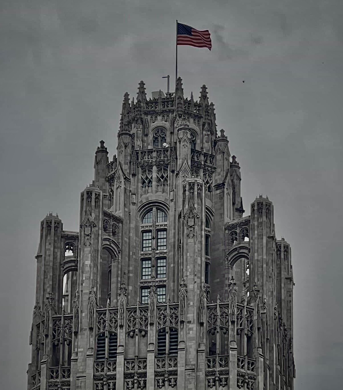 The gothic crown of Tribune Tower under a grey sky, flag flying