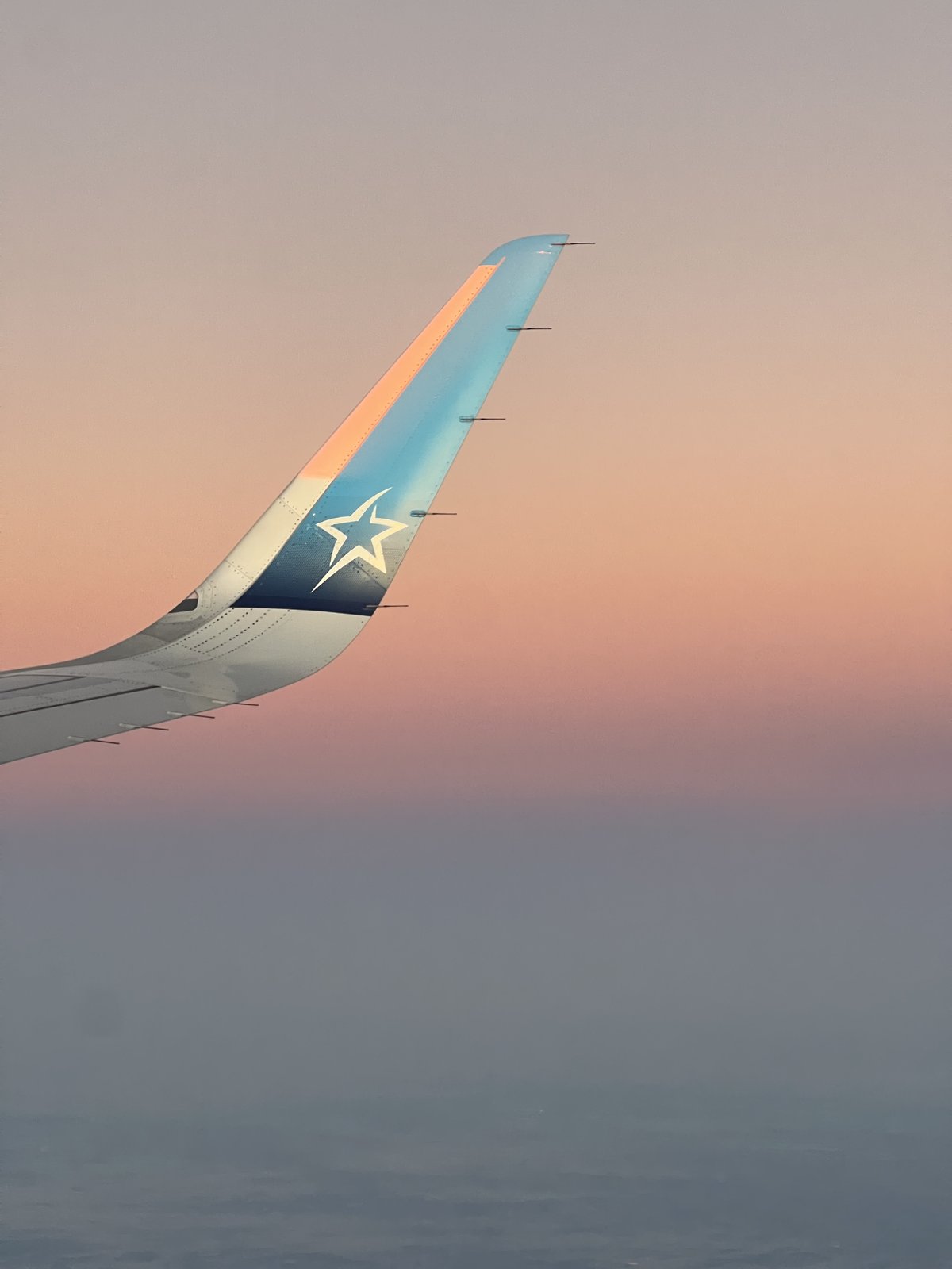 An Air Transat winglet against a layered sunset sky at altitude